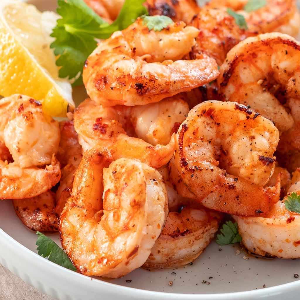 A bowl of fresh, peeled prawns, ready for cooking. The prawns are clean and have a vibrant, pinkish-orange hue, indicating freshness. They are neatly arranged in the bowl, with their tails intact, showcasing their plump and succulent texture.