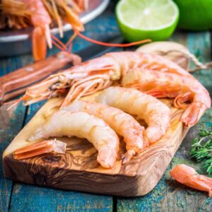 Peeled Argentinian prawns on a wooden board with lime and herbs in the background.