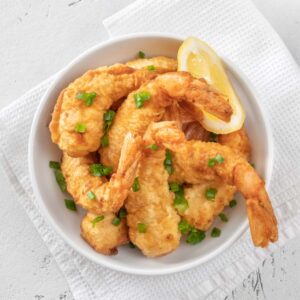 A bowl of golden-brown tempura prawns garnished with green onions and lemon.