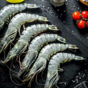 Raw black tiger prawns with stripes on a slate, with salt, tomatoes, and lemon oil.