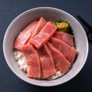 A bowl of sashimi tuna belly, on a bed of rice with some herbs.